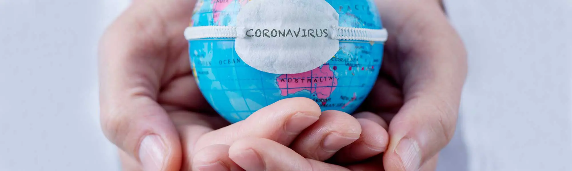 Close up of hands with Coronavirus lable around mini globe